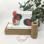 Load image into Gallery viewer, pretty protea birthday card card sits on two paper boxes besides a roll of twine and a potted plant
