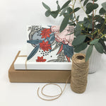Load image into Gallery viewer, tropical floral card sits on two paper boxes besides a roll of twine and a potted plant
