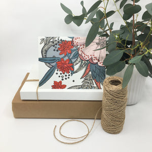 tropical floral card sits on two paper boxes besides a roll of twine and a potted plant
