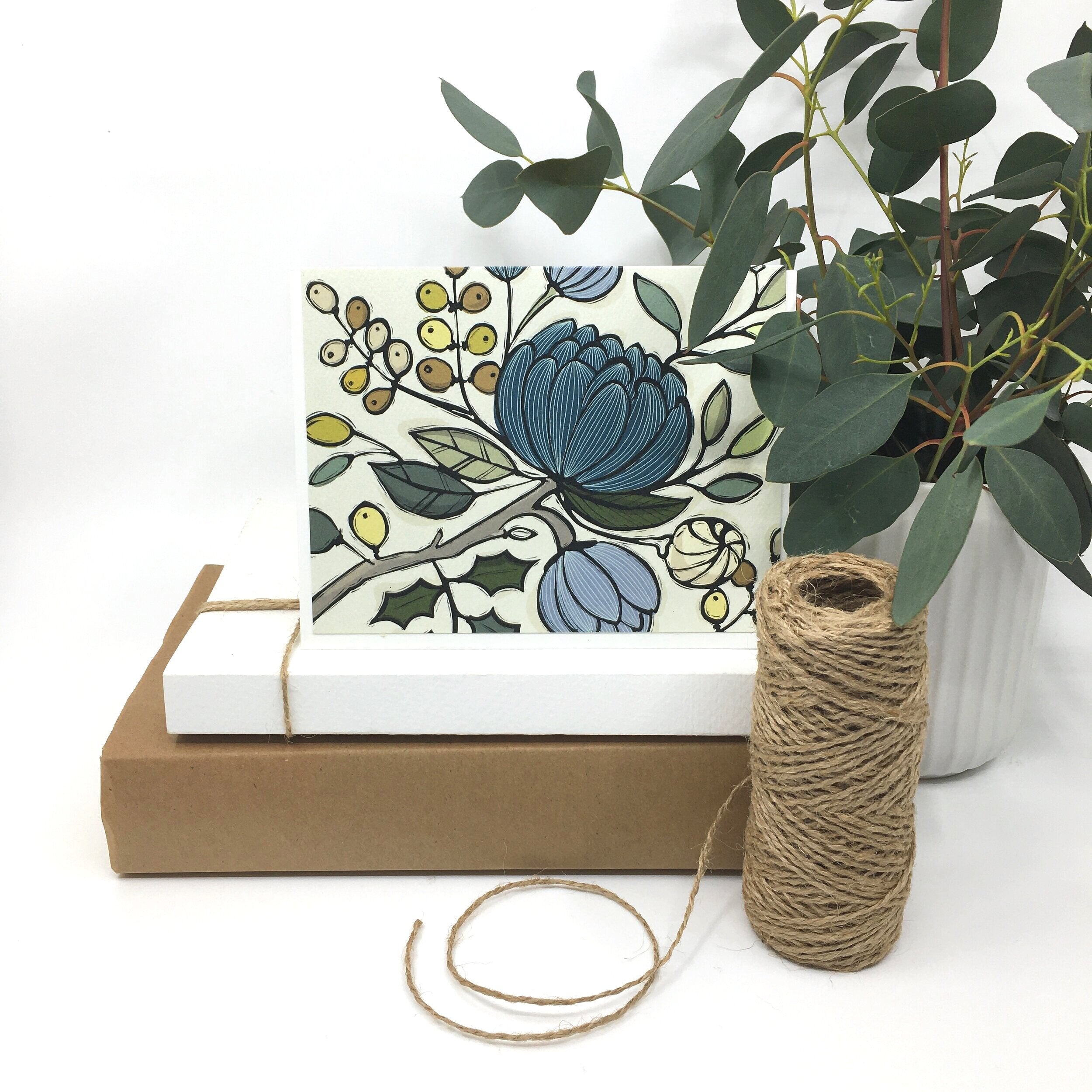 the Mediterranean floral card card sits on two paper boxes besides a roll of twine and a potted plant