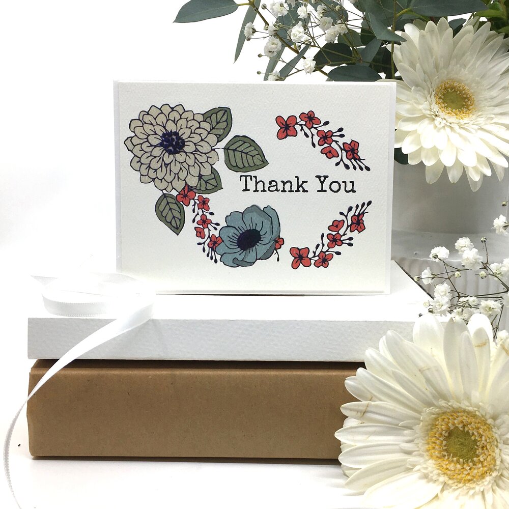 the Japanese floral design thank you card sits on two paper boxes besides two white daisies