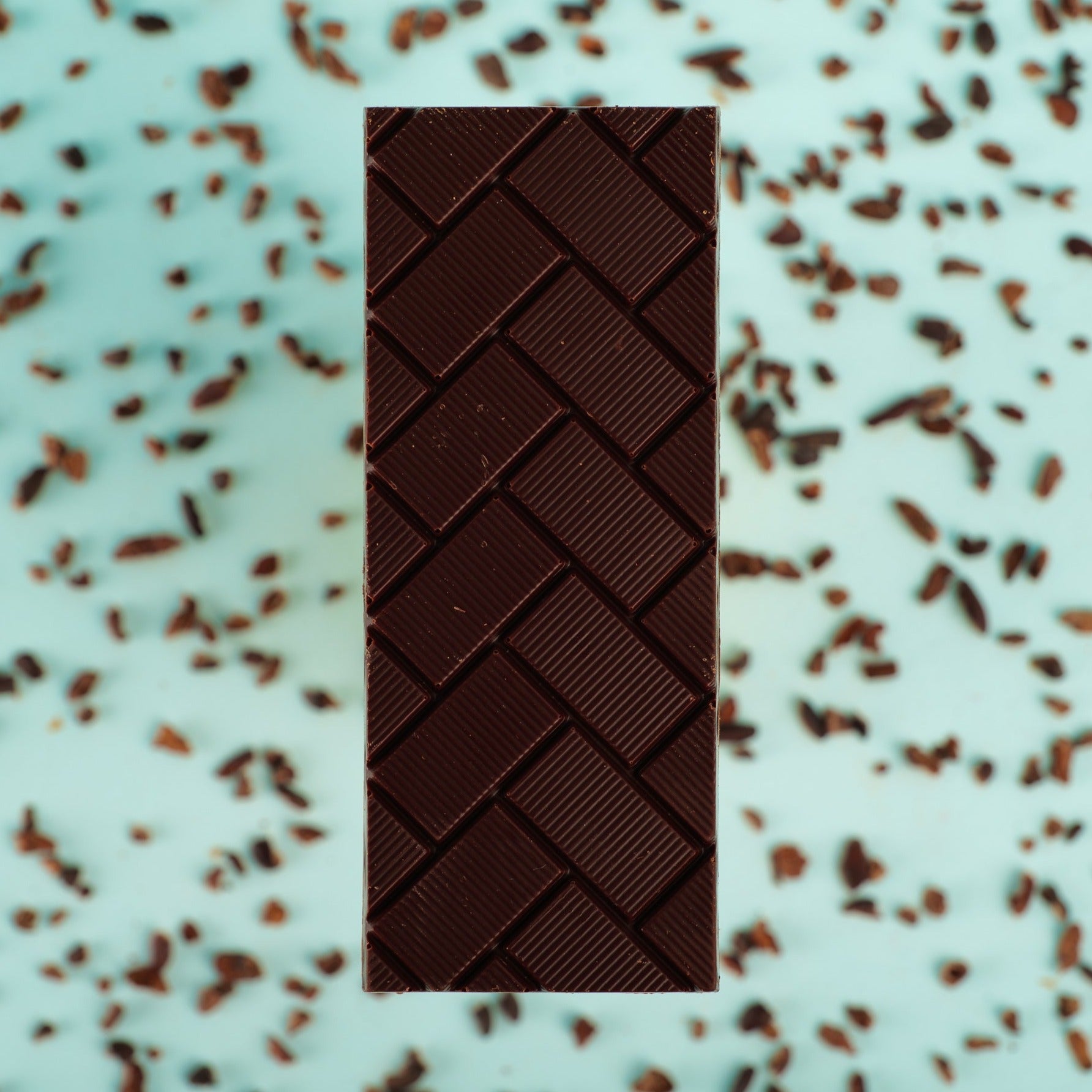 a Colombian dark chocolate bar lies on a blue background with cocoa nibs scattered around