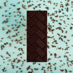 Load image into Gallery viewer, the Tanzania bar lies on a blue background surrounded by cocoa nibs

