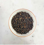 Load image into Gallery viewer, Dried black tea leaves in a white bowl on a marble surface
