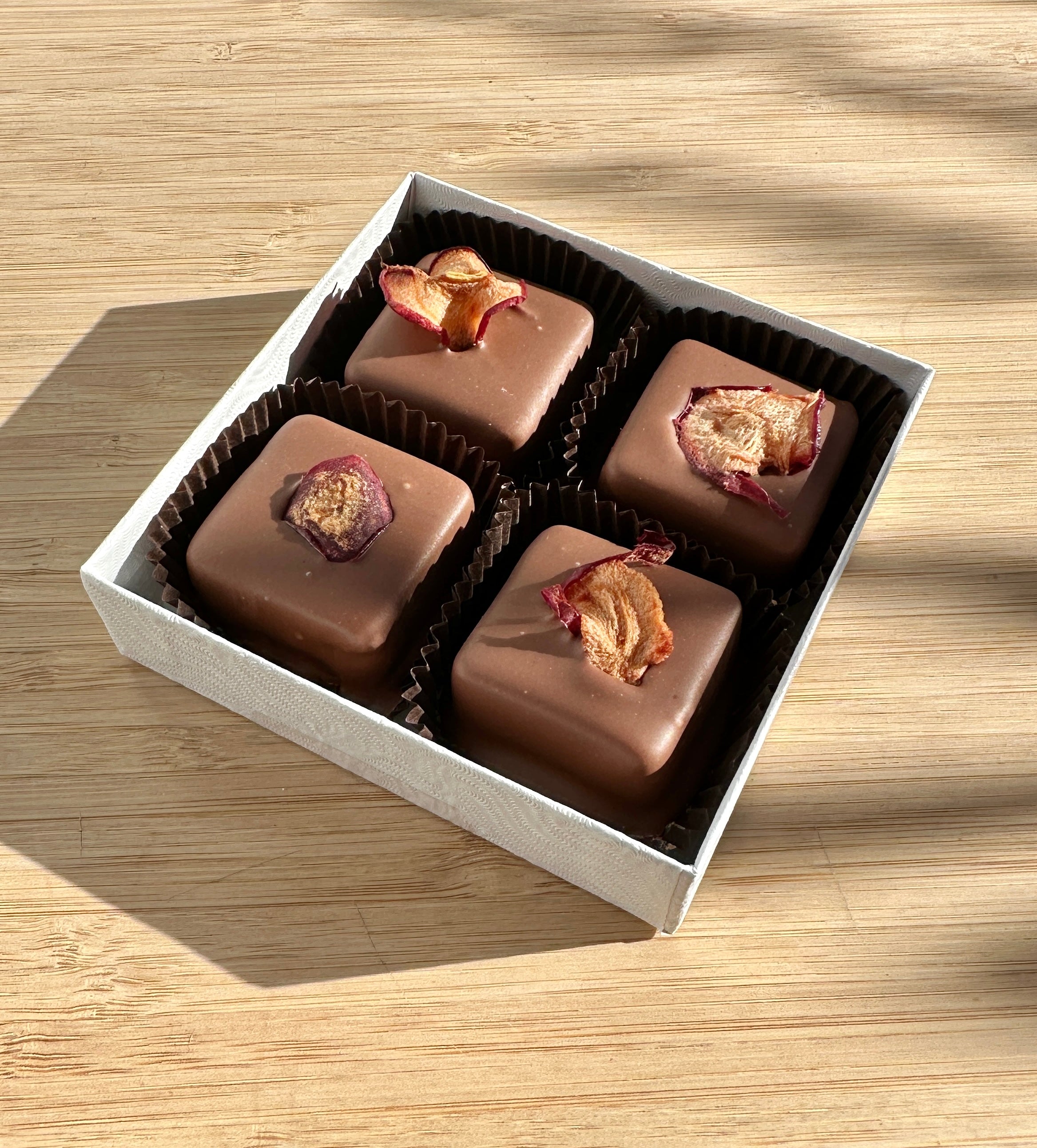 Box of chocolate caramels with pieces of dried apple on a wooden surface