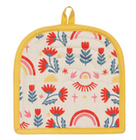 Load image into Gallery viewer, cream quilted potholder with mustard-yellow edging and hanging loop, featuring a colourful folk-art print of red and blue flowers, pink and yellow rainbows, and sun motifs
