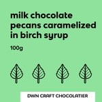 Load image into Gallery viewer, Green label with text and leaf icons for milk chocolate pecans caramelized in birch syrup by DWN Craft Chocolatier.
