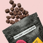 Load image into Gallery viewer, pieces of dark chocolate candied ginger fall out of a DWN Chocolate pouch onto a light pink background
