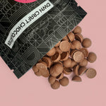 Load image into Gallery viewer, chocolate chips spilling out of a black and white branded bag on a pink background
