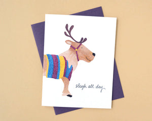 Card with a reindeer wearing a colorful sweater and 'sligh all day' text on a beige background