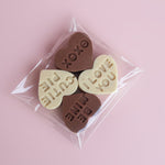 Load image into Gallery viewer, milk chocolate and milk chocolate conversation hearts on a light pink background
