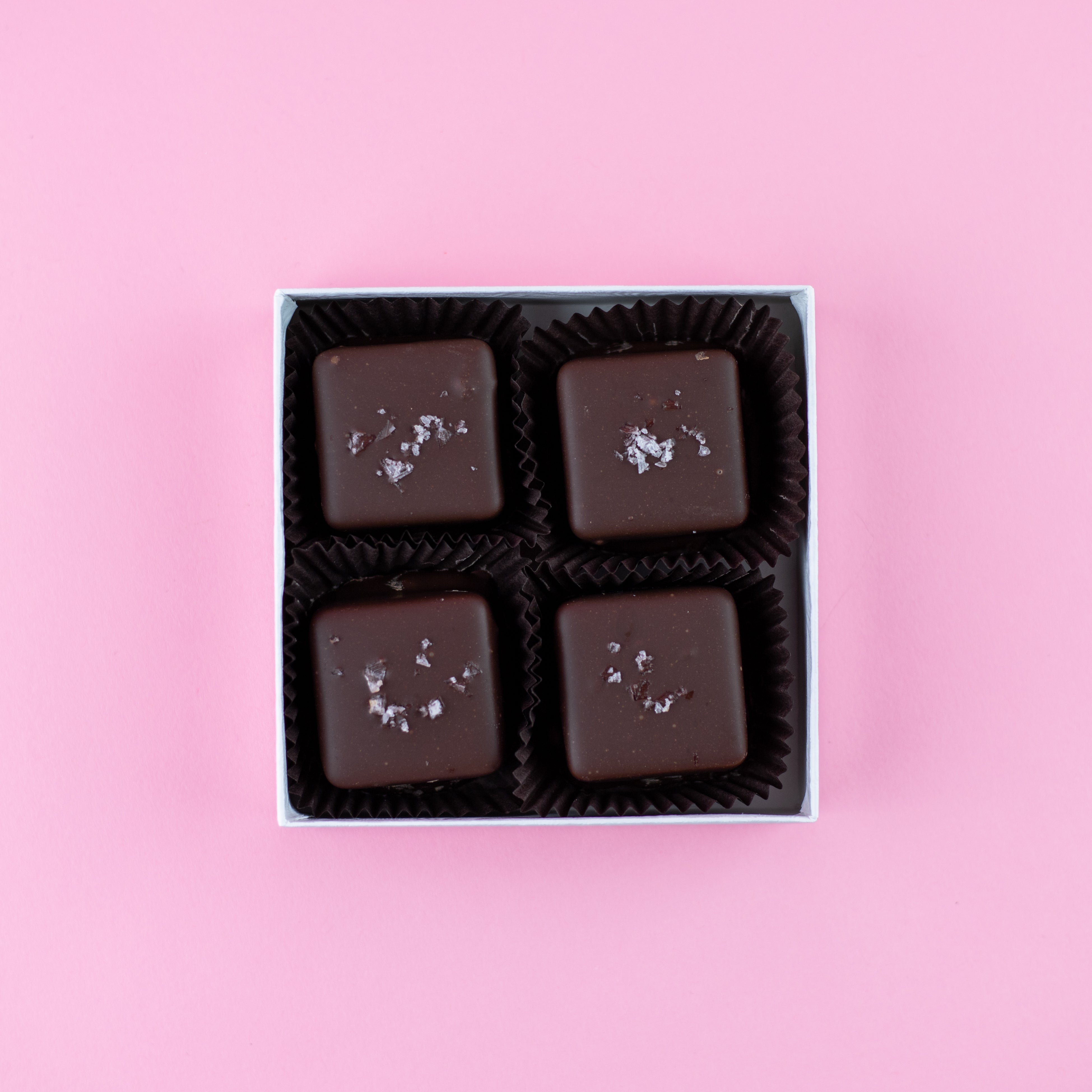 four dark chocolate salted caramels in a box on a pink background