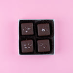 Load image into Gallery viewer, four dark chocolate salted caramels in a box on a pink background
