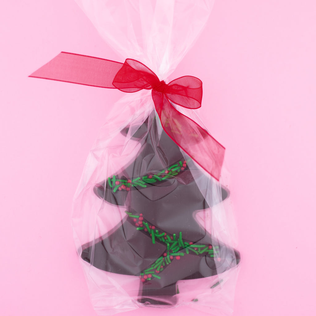 dark chocolate tree with green and red sprinkles in a clear bag with a red bow on a pink background