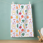 Load image into Gallery viewer, white tea towel featuring a colourful, whimsical print of smiling cartoon fruits, vegetables, and breakfast foods, including tomatoes, carrots, broccoli, bananas, cucumbers, strawberries, and fried eggs on toast hanging on a clothesline in front of a green background
