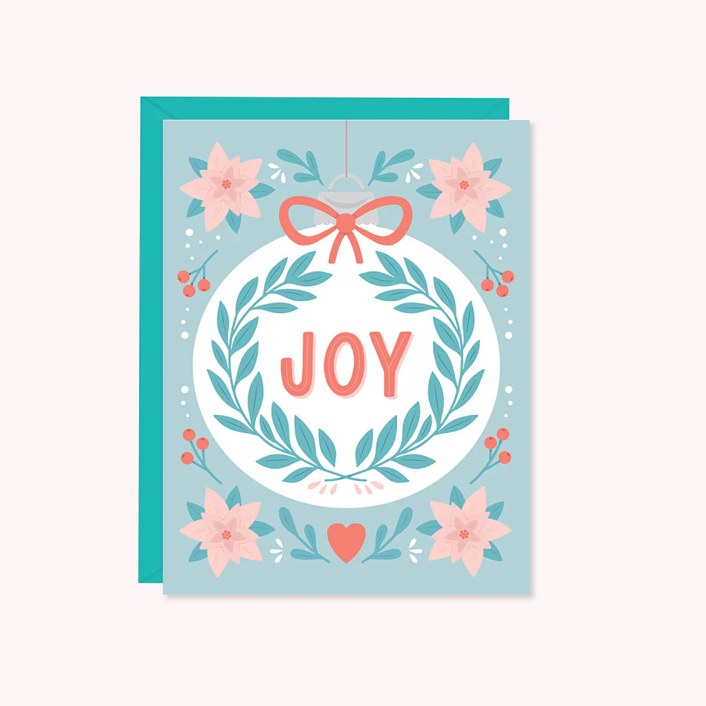 a white ornament with the word Joy is surrounded by Christmas florals
