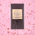Load image into Gallery viewer, lilac dark chocolate bar with a yellow label on a pink background
