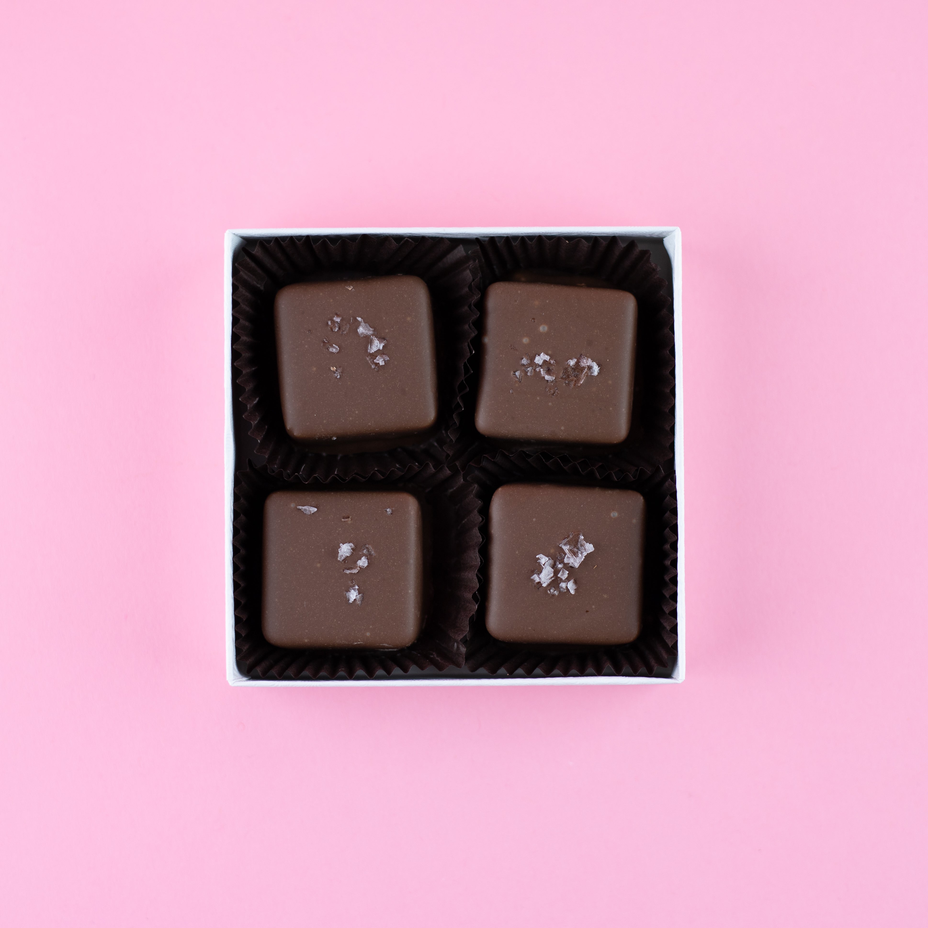 four milk chocolate salted caramels in a box on a pink background