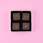 Load image into Gallery viewer, four milk chocolate salted caramels in a box on a pink background
