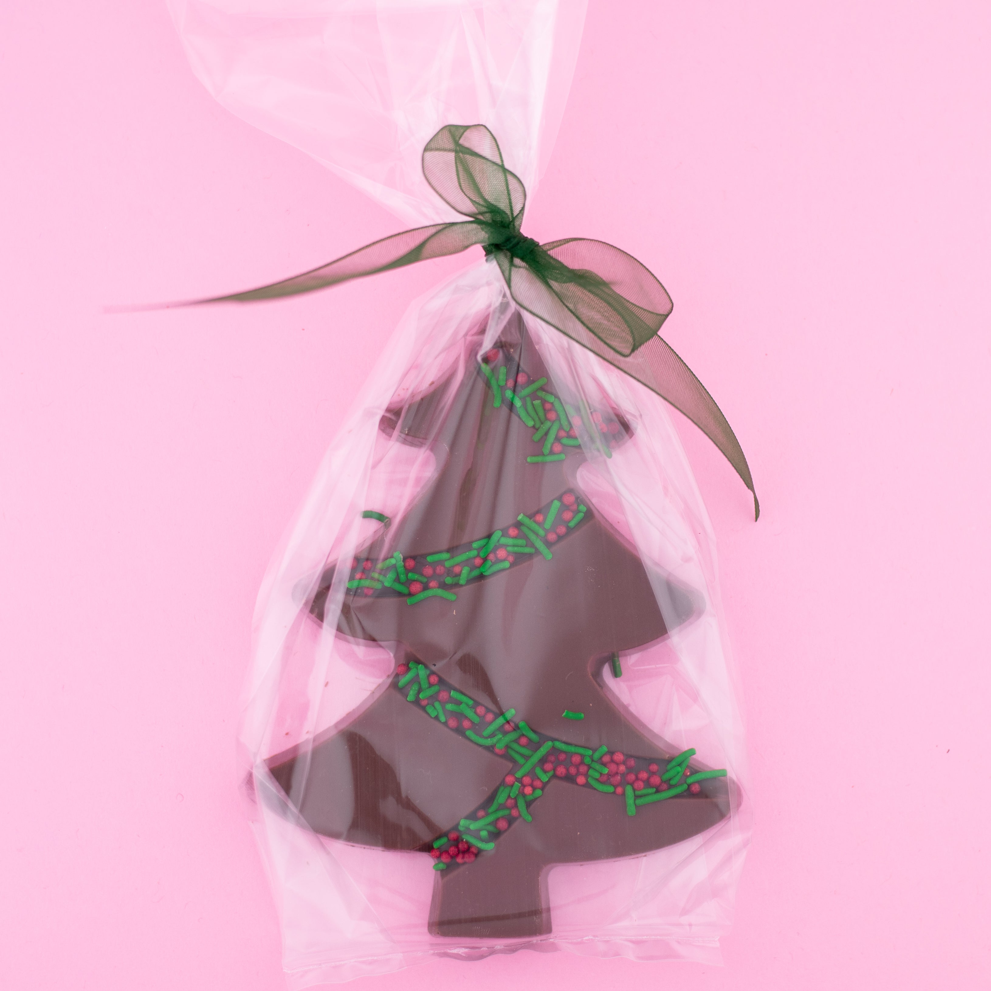 milk chocolate tree with green and red sprinkles in a clear bag with a red bow on a pink background