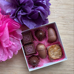 Load image into Gallery viewer, seven piece bonbon collection in a white box on a wooden board background with decorative tissue flowers
