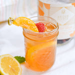 Load image into Gallery viewer, a glass full with the peach berry sangria cocktail, with a raspberry and a slice of peach
