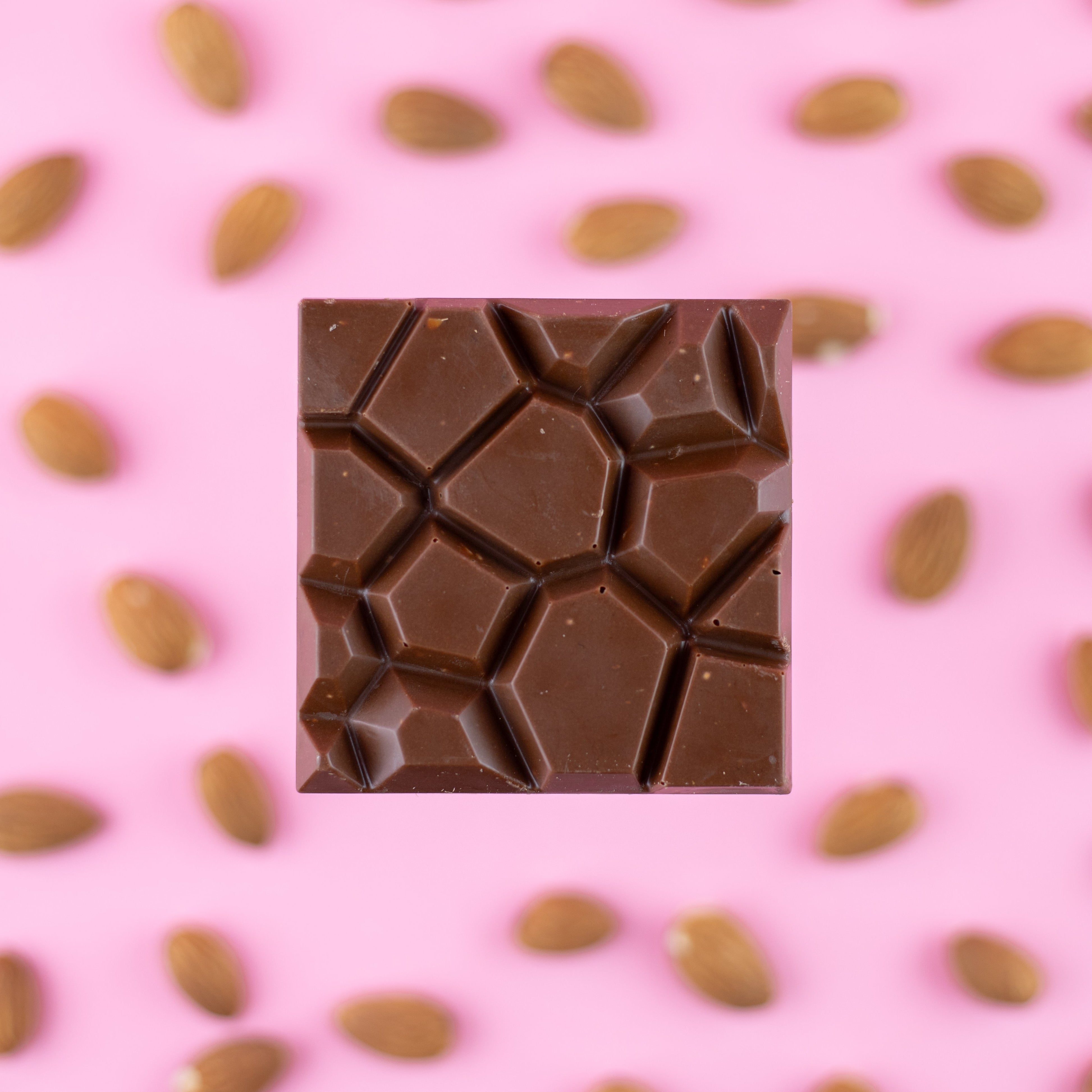 milk chocolate with salted almonds chocolate bar on a pink background with almonds