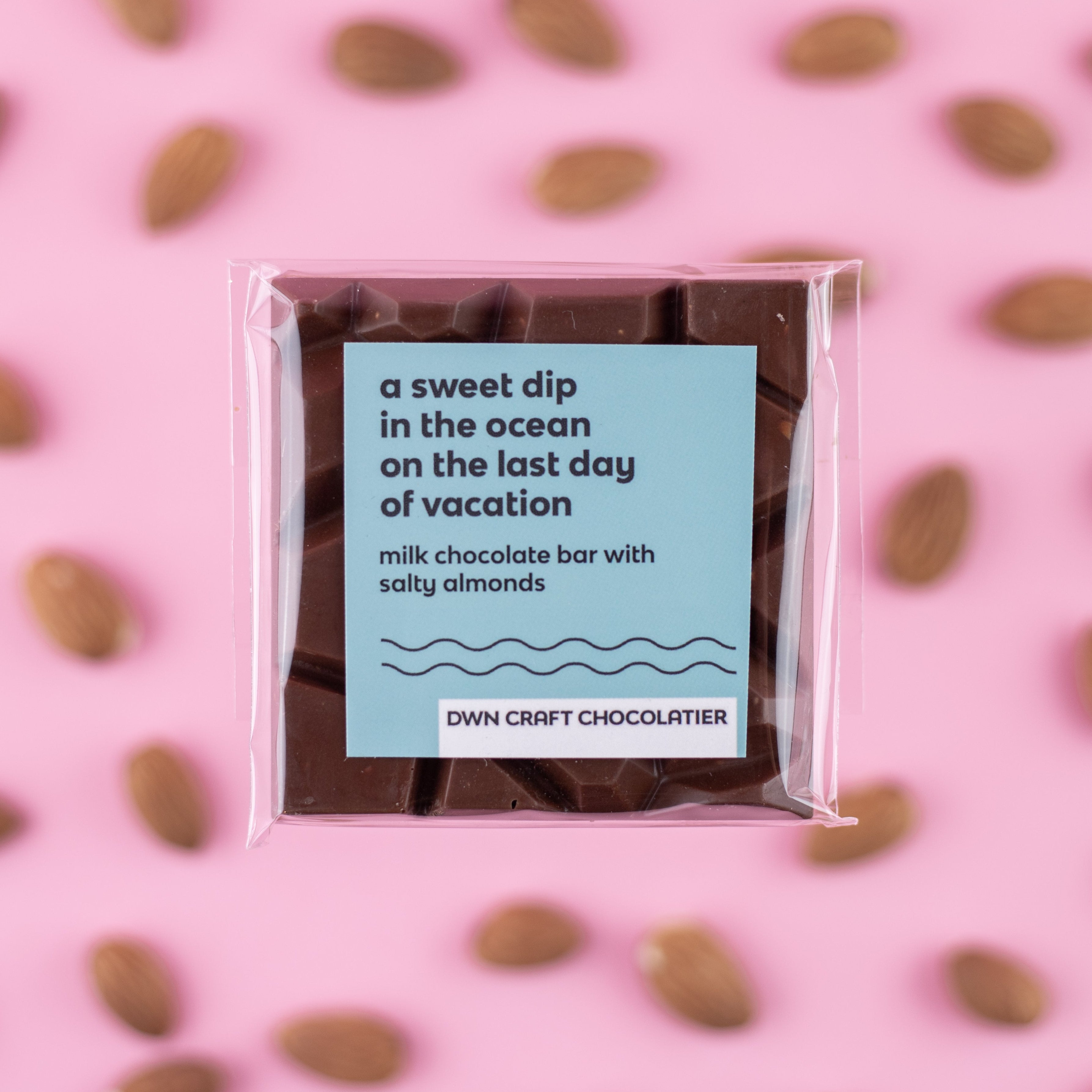 Milk chocolate bar with salty almonds in clear packaging on a pink background with almonds