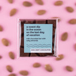 Load image into Gallery viewer, Milk chocolate bar with salty almonds in clear packaging on a pink background with almonds
