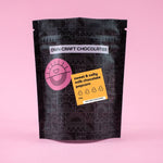 Load image into Gallery viewer, A black stand-up pouch of DWN Craft Chocolatier 'sweet &amp; salty milk chocolate popcorn' on a solid pink background
