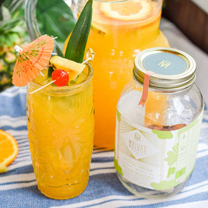 tropical sangria cocktail infusion kit jar next to a glass full with the cocktail with orange juicy and a cherry, a slice of pineapple and an umbrella on top