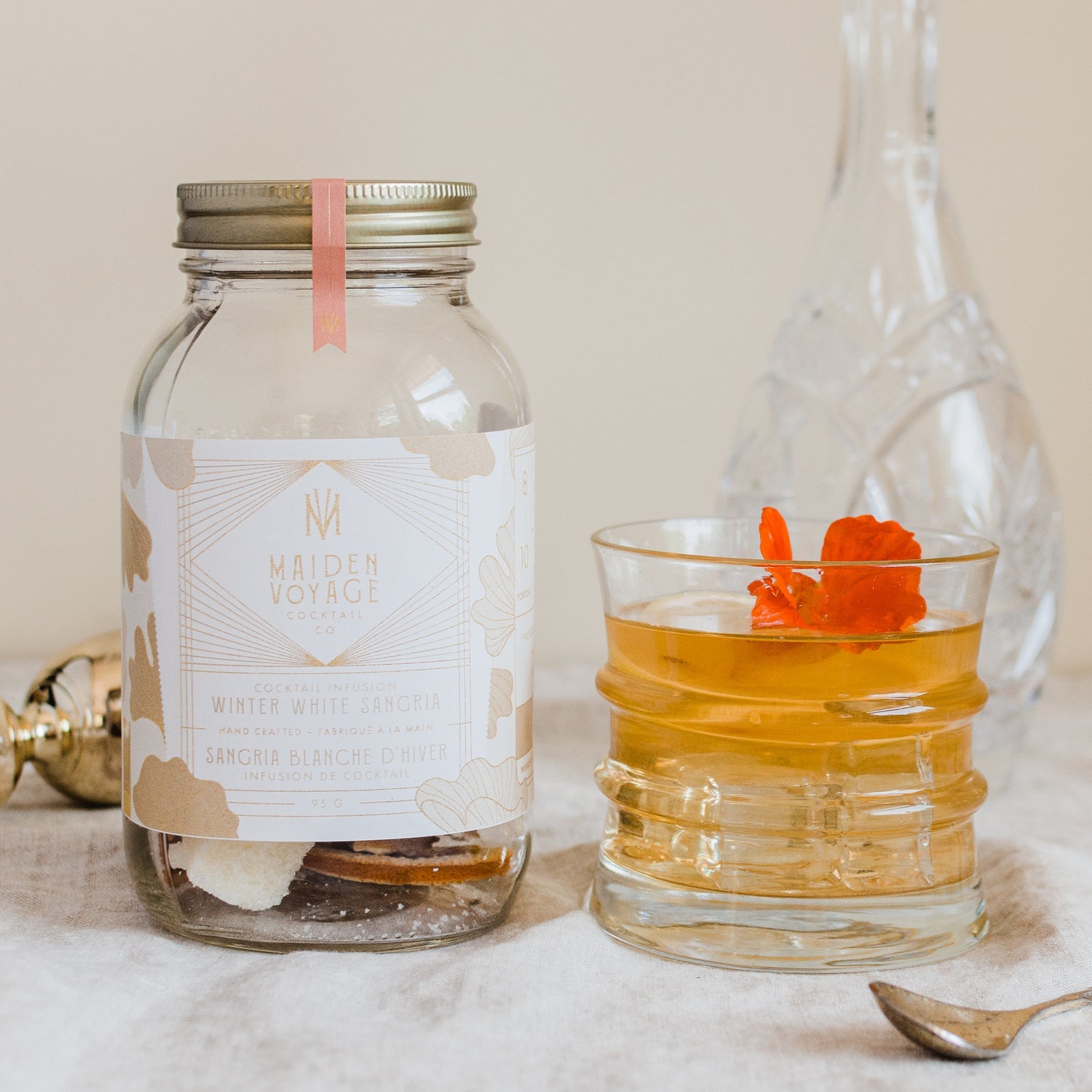 winter white sangria cocktail infusion kit jar next to a rick glass full with the coctail and an orange flower on top