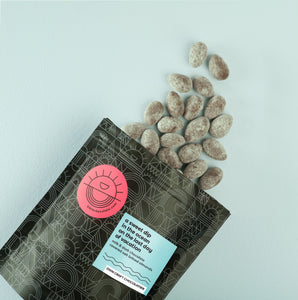a pouch of chocolate-covered salted almonds fall out of the packaging onto a blue background