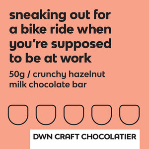 Label for hazelnut milk chocolate bar has a bright orange background with black text that reads, "sneaking out for a bike ride when you're supposed to be at work. 50g / crunchy hazelnut milk chocolate bar. DWN Craft Chocolatier."