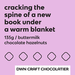 buttermilk chocolate hazelnuts label with black text and a lavender background that reads, "cracking the spine of a new book under a warm blanket. 135g / buttermilk chocolate hazelnuts. DWN Craft Chocolatier"