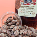 Load image into Gallery viewer, maple dusted almonds are falling out of a small jar in front of a bottle of maple syrup
