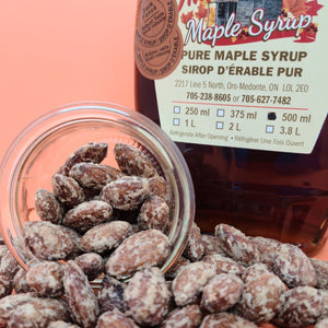 maple dusted almonds are falling out of a small jar in front of a bottle of maple syrup