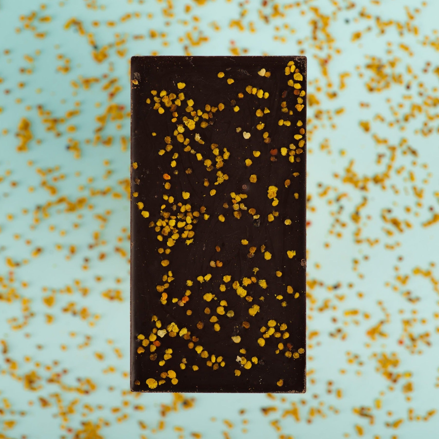 lilac dark chocolate bar lies on a bed of bee pollen with the backside of the bar showing the sprinkle of bee pollen