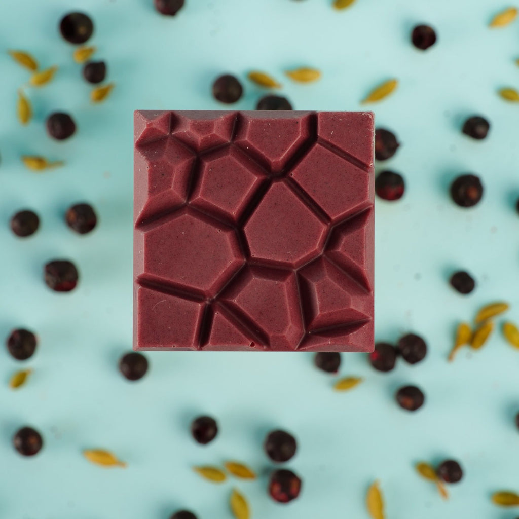 a cassis cardamom bar on a bed of black currants and cardamom pods on a blue background