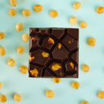 Load image into Gallery viewer, a caramelized hazelnut bar on a bed of hazelnuts on a blue background
