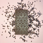Load image into Gallery viewer, a dark chocolate bar on a light pink background with cocoa nibs scattered around

