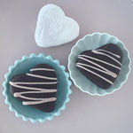 Load image into Gallery viewer, two dark chocolate-covered marshmallow and one plain strawberry marshmallow lie on a pink background
