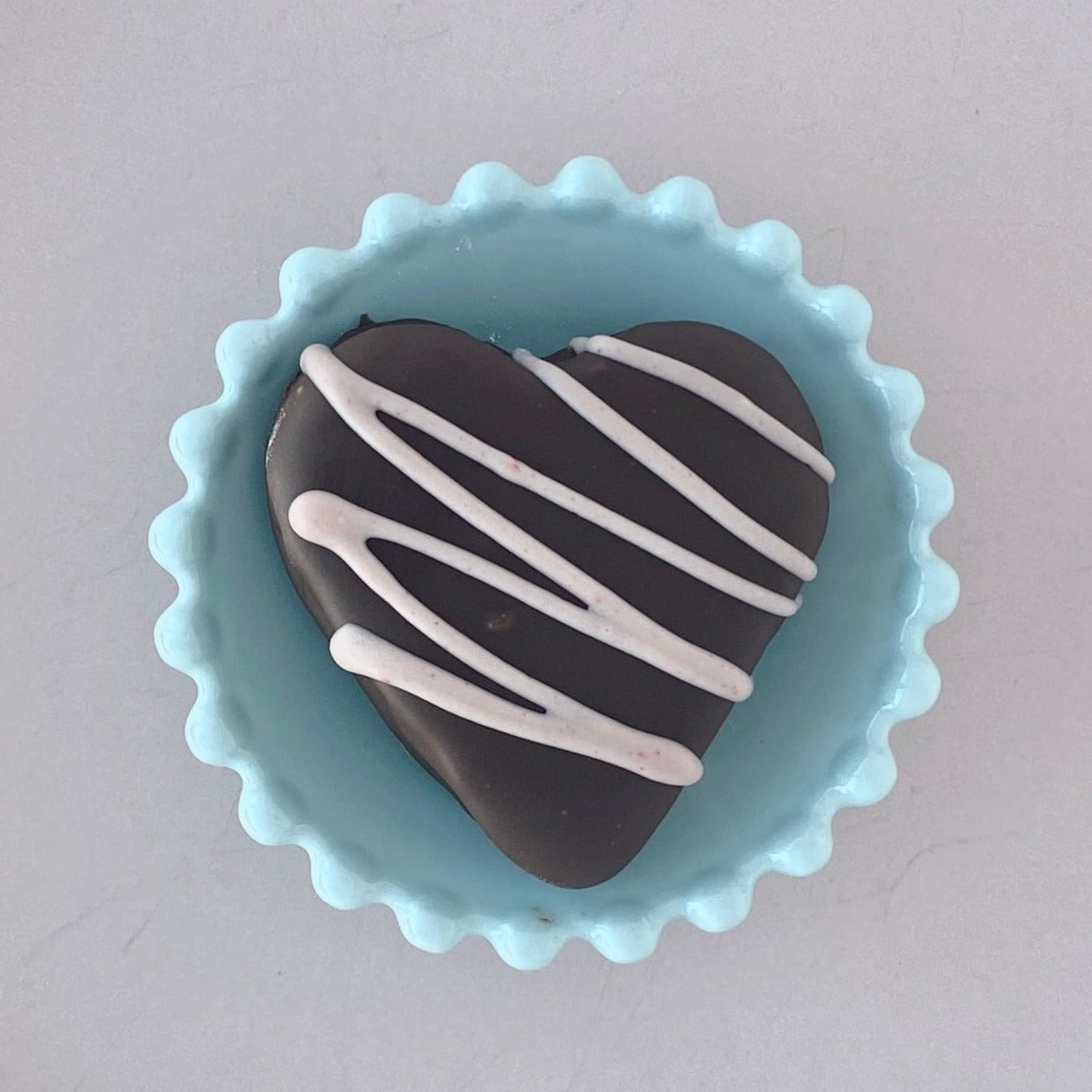one dark chocolate-covered strawberry marshmallow sits in a blue scalloped bowl with pink chocolate drizzle