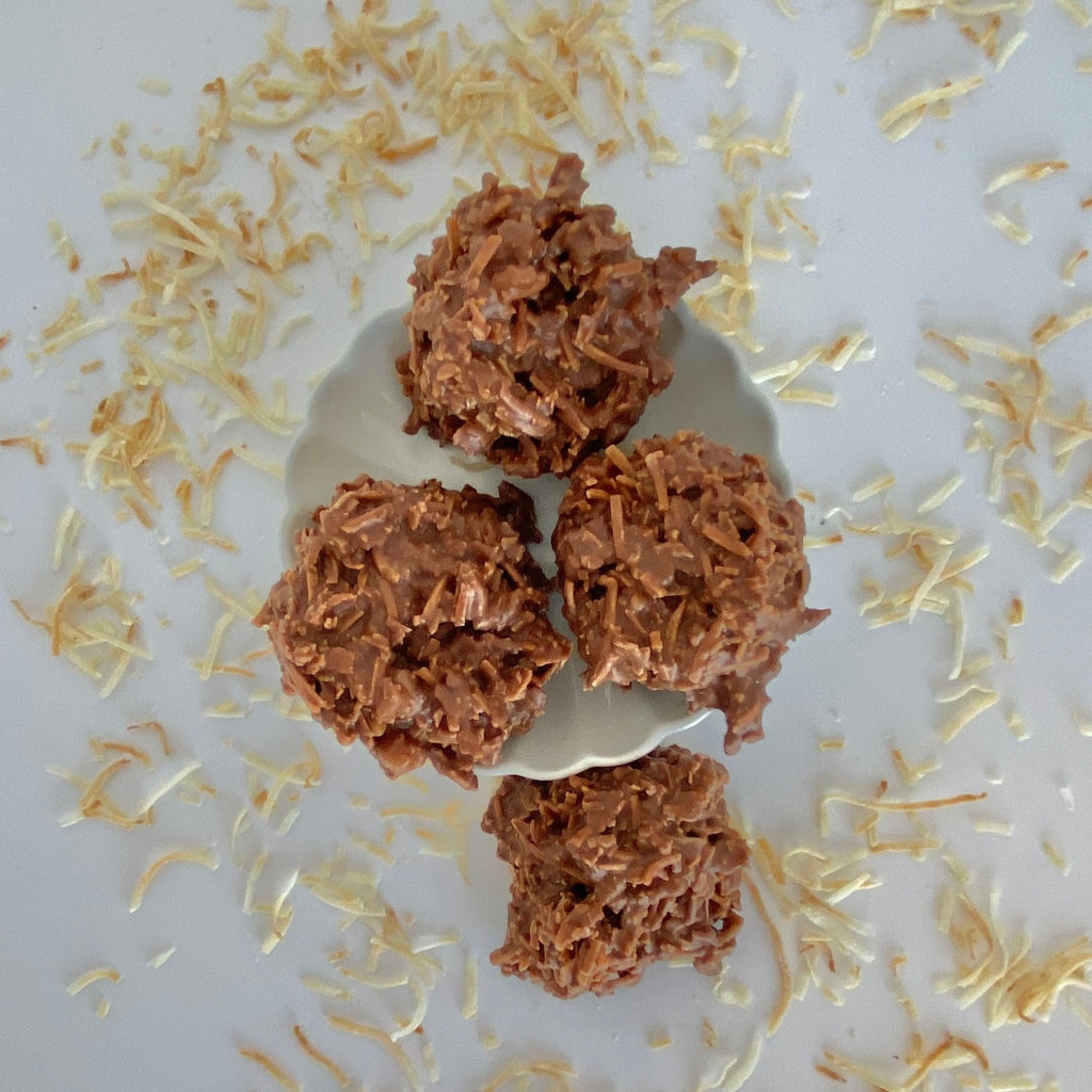 four coconut clusters sit on a white background with toasted coconut scattered around