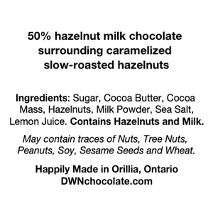 Ingredients list for caramelized hazelnut bar reads, "50% hazelnut milk chocolate  surrounding caramelized  slow-roasted hazelnuts   Ingredients: Sugar, Cocoa Butter, Cocoa  Mass, Hazelnuts, Milk Powder, Sea Salt,  Lemon Juice. Contains Hazelnuts and Milk. May contain traces of Nuts, Tree Nuts,  Peanuts, Soy, Sesame Seeds and Wheat. Happily Made in Orillia, Ontario DWNchocolate.com"