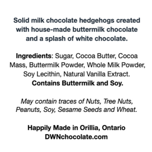 Black text that reads, "Solid milk chocolate hedgehogs created  with house-made buttermilk chocolate  and a splash of white chocolate. Ingredients: Sugar, Cocoa Butter, Cocoa  Mass, Buttermilk Powder, Whole Milk Powder,  Soy Lecithin, Natural Vanilla Extract.  Contains Buttermilk and Soy. May contain traces of Nuts, Tree Nuts,  Peanuts, Soy, Sesame Seeds and Wheat. Happily Made in Orillia, Ontario DWNchocolate.com"