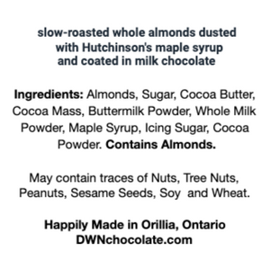 a white ingredient label with black text reads, "slow-roasted whole almonds dusted in Hutchinson's maple syrup and coated in milk chocolate. Ingredients: Almonds, Sugar, Cocoa Butter, Cocoa Mass, Buttermilk Powder, Whole Milk Powder, Maple Syrup, Icing Sugar, Cocoa Powder. Contains Almonds. May contain traces of Nuts, Tree Nuts, Peanuts, Sesame Seeds, Soy and Wheat. Happily Made in Orillia, Ontario. DWNchocolate.com."