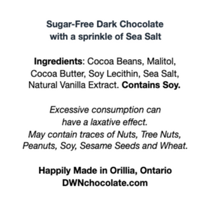 white ingredient label with black text that reads, "Sugar-Free Dark Chocolate with a sprinkle of Sea Salt Ingredients: Cocoa Beans, Malitol,  Cocoa Butter, Soy Lecithin, Sea Salt,  Natural Vanilla Extract. Contains Soy. Excessive consumption can  have a laxative effect. May contain traces of Nuts, Tree Nuts,  Peanuts, Soy, Sesame Seeds and Wheat. Happily Made in Orillia, Ontario DWNchocolate.com"
