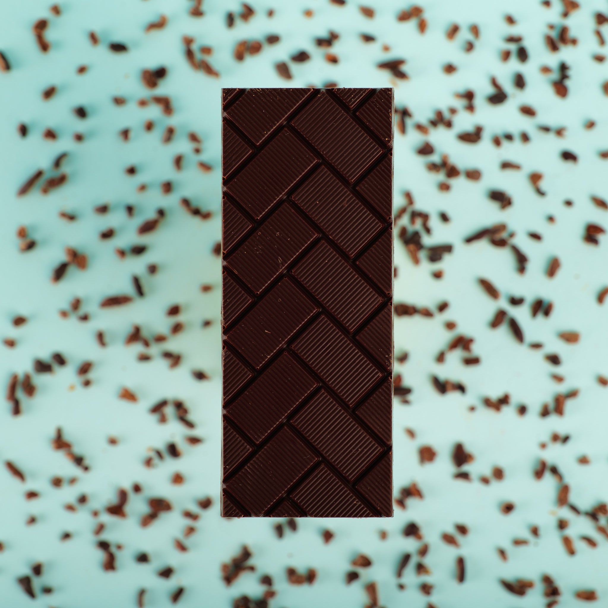 the Tanzania bar lies on a blue background surrounded by cocoa nibs