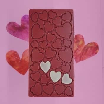 a raspberry toffee bar lies on a pink background with three paper hearts